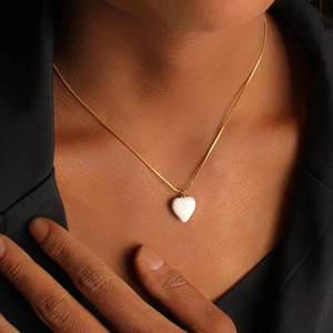 Close-up of a minimalist gold snake chain necklace with a white heart pendant on a model