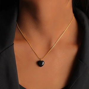 Detail view of 18K gold snake chain with a polished black heart pendant on a model
