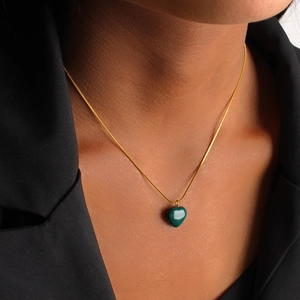 Detail of a green heart pendant on a gold snake chain necklace worn with a black blazer
