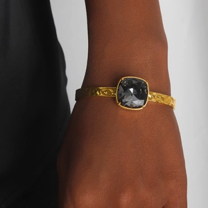 Detail of gold-plated hammered cuff bracelet with a square faceted dark grey crystal