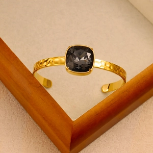 Detailed macro of golden hammered C-shaped bangle featuring a large square grey crystal