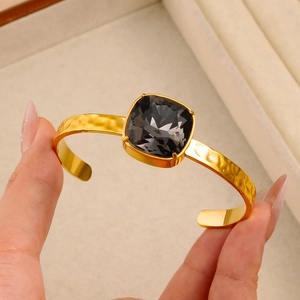 Golden C-shaped open bracelet with a large square faceted grey crystal on hammered metal
