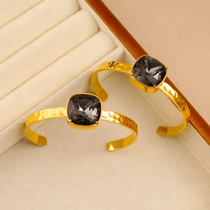 Detailed close-up of 18K gold-plated C-shaped cuff with faceted square black crystal