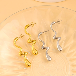 Detalle de pendientes de ondas irregulares en oro y plata sobre una bandeja de vidrio