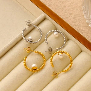 Dettaglio di orecchini con perle a forma di C in finiture oro e argento su velluto