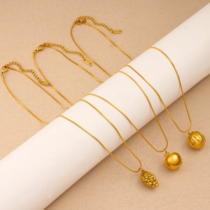 Detailed view of three gold fruit pendant necklaces on a white display cylinder