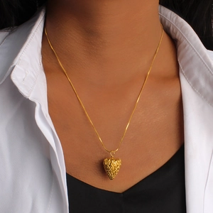 Detail of a gold strawberry pendant necklace with diamond texture on a white shirt model