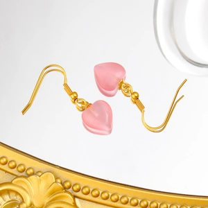 Détail de boucles d'oreilles crochet dorées avec pendentifs cœur en œil de chat rose
