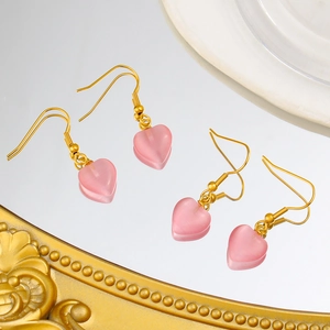 Détail de boucles d'oreilles cœur en opale rose avec crochets dorés sur miroir luxe