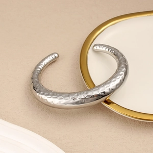 Detalle de un brazalete ancho y abierto en forma de C con acabado plateado de textura martillada