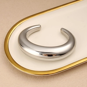 Detalle de brazalete plateado minimalista en forma de C con acabado de espejo pulido