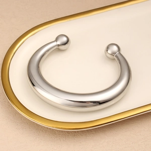 Vista detallada del brazalete de acero inoxidable pulido en forma de C sobre bandeja