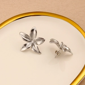 Macro shot of polished silver flower earrings placed on a luxury white ceramic plate