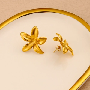 Detailed macro of gold matte five-petal flower earrings on a white porcelain dish