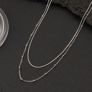 Detail einer silbernen Doppelkette mit Schlangenkette und glänzender Perlenkette für Damen