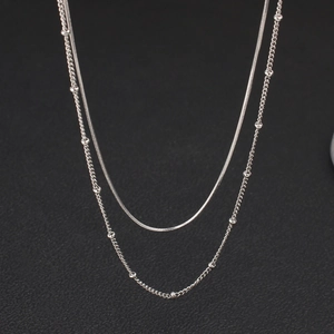 Detail einer silbernen Doppelkette mit flacher Schlangenkette und feiner Perlenkette
