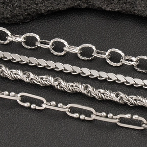 Detailed close-up of four geometric stainless steel chain styles on black leather background