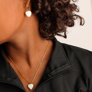 Detail of elegant gold necklace and earrings set with white heart enamel pendants on model