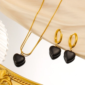 Close-up of golden necklace and hoop earrings with black heart pendants on champagne silk