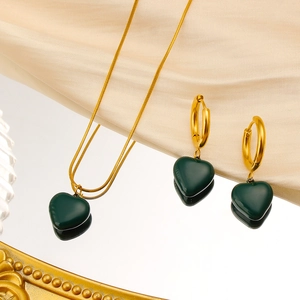 Macro shot of green heart pendant jewelry set with golden snake chain on silk cloth