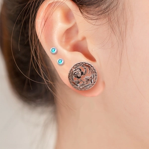Détail macro d'un écarteur d'oreille ajouré en or rose avec motif floral et perles fines