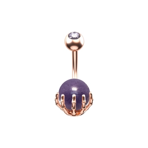 Detalle de un piercing de ombligo en oro rosa con mano de esqueleto y piedra violeta