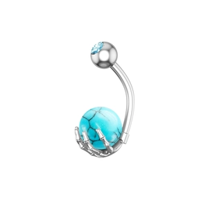 Detalle de una mano de esqueleto sosteniendo una cuenta turquesa en un piercing de ombligo