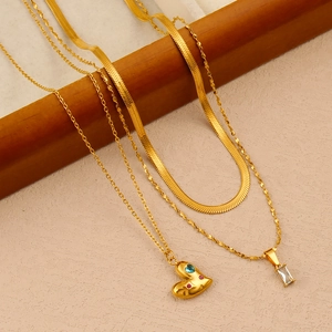 Dettaglio di collane a strati in oro 18K con ciondoli a cuore e zirconi su barra di legno