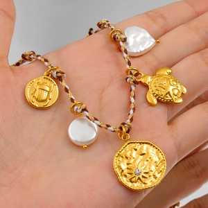 Detalle de pulsera tejida con tortuga dorada, perla de corazón y colgante de sol