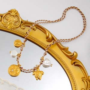 Detalle de collar bohemio con dijes dorados, tortuga y perla en forma de corazón