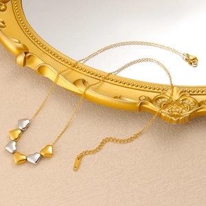 Nahaufnahme von Herzanhängern an Goldkette mit K18-Etikett auf goldenem Spiegelrahmen