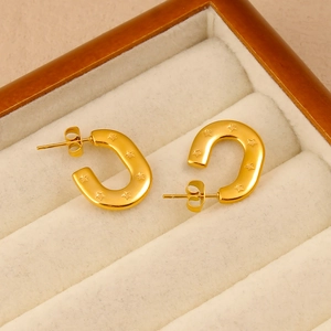 Détail de boucles d'oreilles dorées en U avec motifs d'étoiles gravés sur acier poli