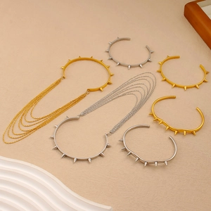 Dettagli di bracciali con borchie punk oro e argento e collane a strati su vassoio deco