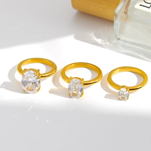 Three gold rings with oval cubic zirconia in four-prong settings on white surface
