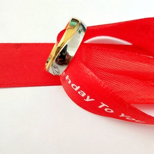 Détail d'une bague bicolore en acier avec diamants sur un ruban d'anniversaire rouge