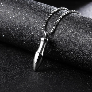 Collier avec pendentif balle en acier titane et chaîne boîte sur fond texturé noir