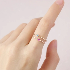 Detail showing two rose gold stainless steel rings with blue and pink rhinestones worn on finger