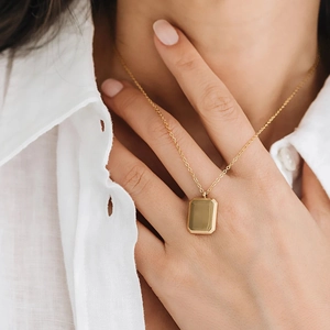 Gold rectangular pendant necklace with serrated edges on a fine chain worn by a model