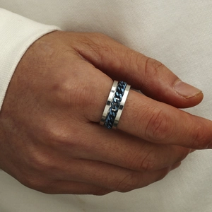 Bague pour homme en acier titane avec chaîne bleue, portée sur la main sur tissu blanc