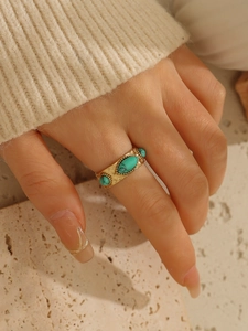 Dettaglio macro di un anello in acciaio dorato 18k con tre pietre turchesi incastonate