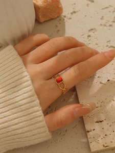 Dettaglio di un anello a infinito dorato 18k con pietra rossa rettangolare su base in pietra
