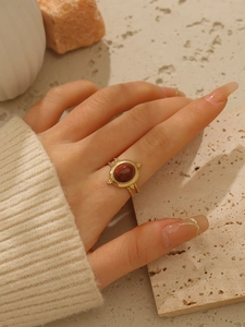 Dettaglio anello in acciaio placcato oro 18k con gemma rossa ovale e bordo con perline