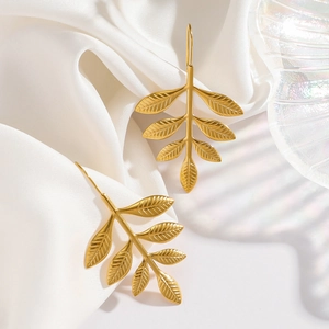 Detailed view of golden leaf earrings with intricate vein textures on white silk