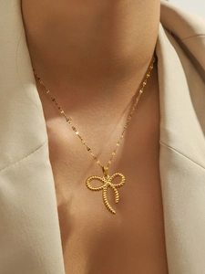 Detail of a vintage bow pendant gold necklace worn on a cream-colored blazer