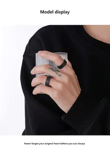 Close-up of matte black minimalist rings worn while holding a striped glass cup
