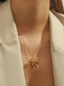 Close-up of golden bow pendant necklace on model with detailed metal texture and fine chain