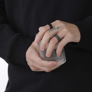 Minimalist matte black ceramic texture rings for couples shown on hand with glass