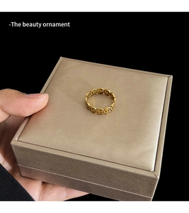 Close-up of golden coin-style ring with square hole patterns in a velvet jewelry box