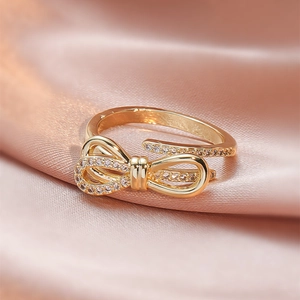 Elegant gold bow ring with sparkling crystals on pink silk background, adjustable open band