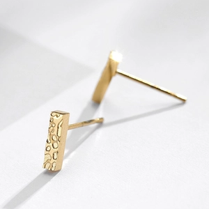 Detail van minimalistische gouden rechthoekige oorknopjes met een moderne gehamerde textuur